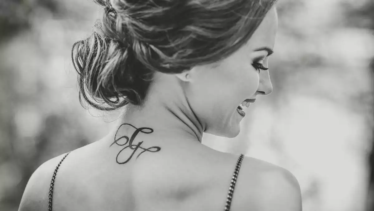 A black and white picture of a woman with her hair up and with a tattoo on her back.