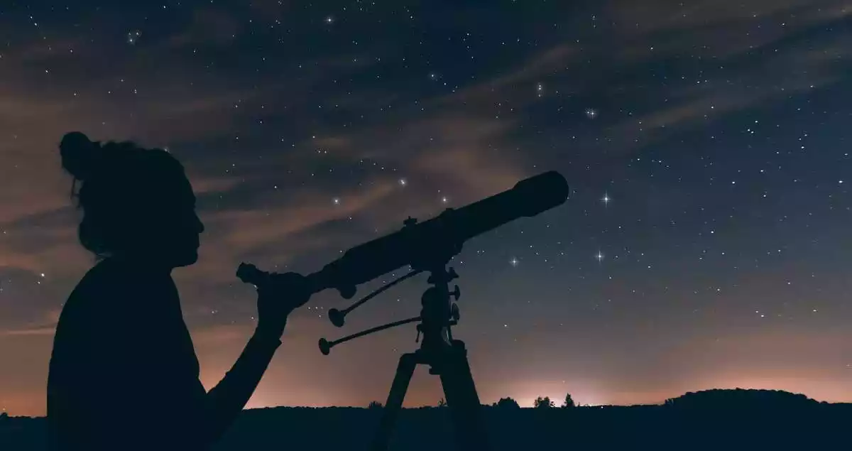 A person with a telescope with the night sky in the background