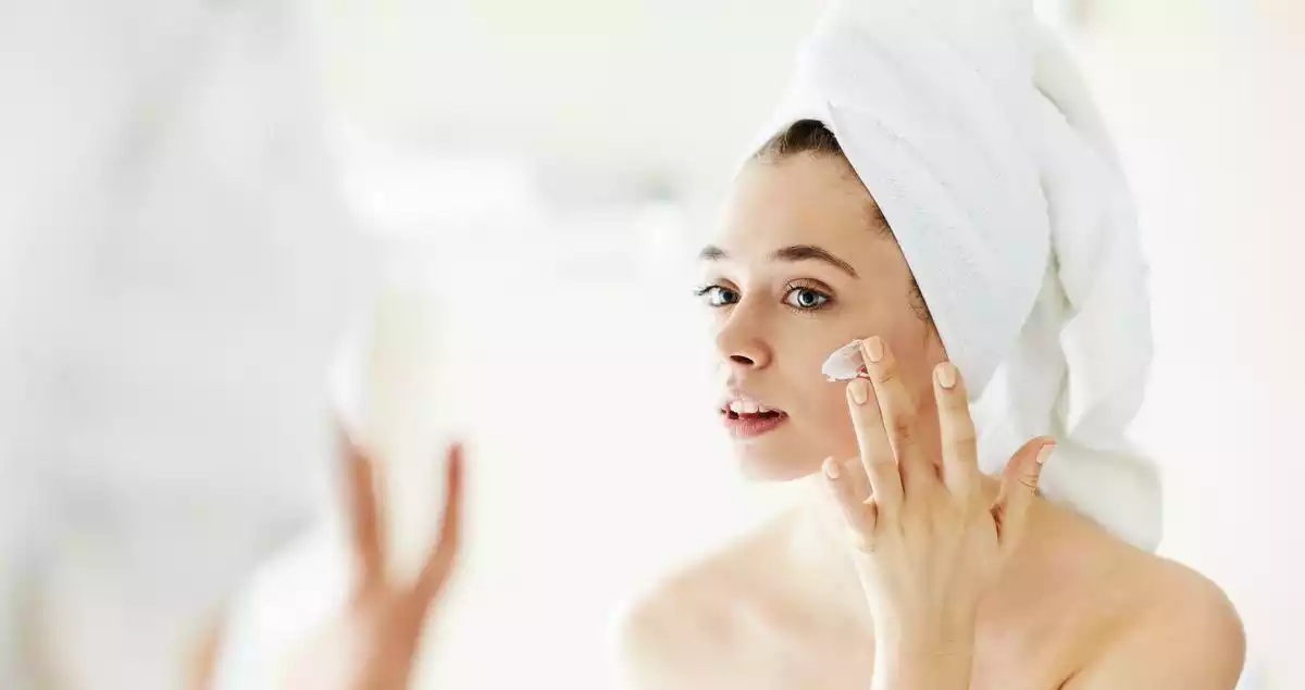 A woman putting some cream on her face after a shower