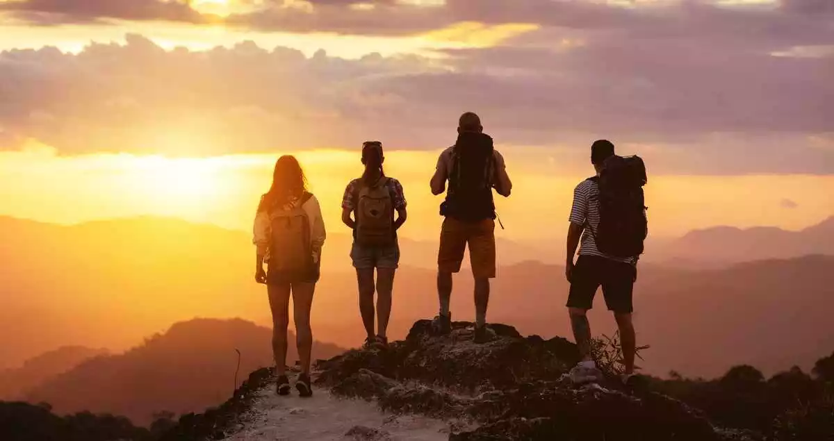 Group of four people's silhouettes stands on mountain top and looks at sunset