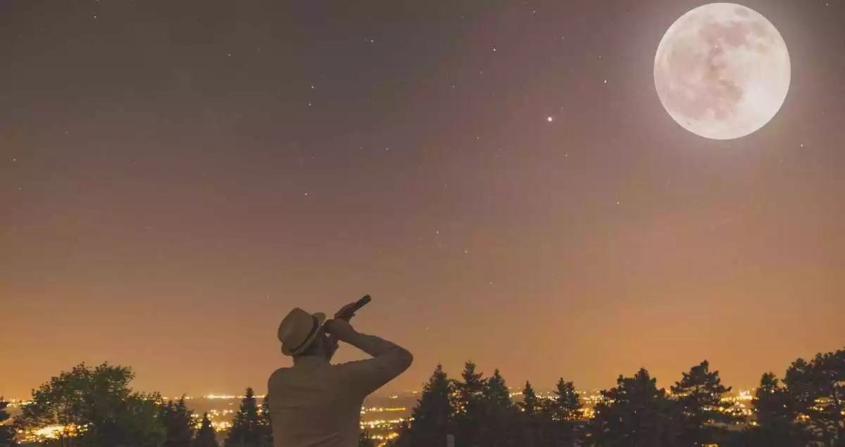 Young man with hat watching full moon and stars by using spyglass. Night scene.