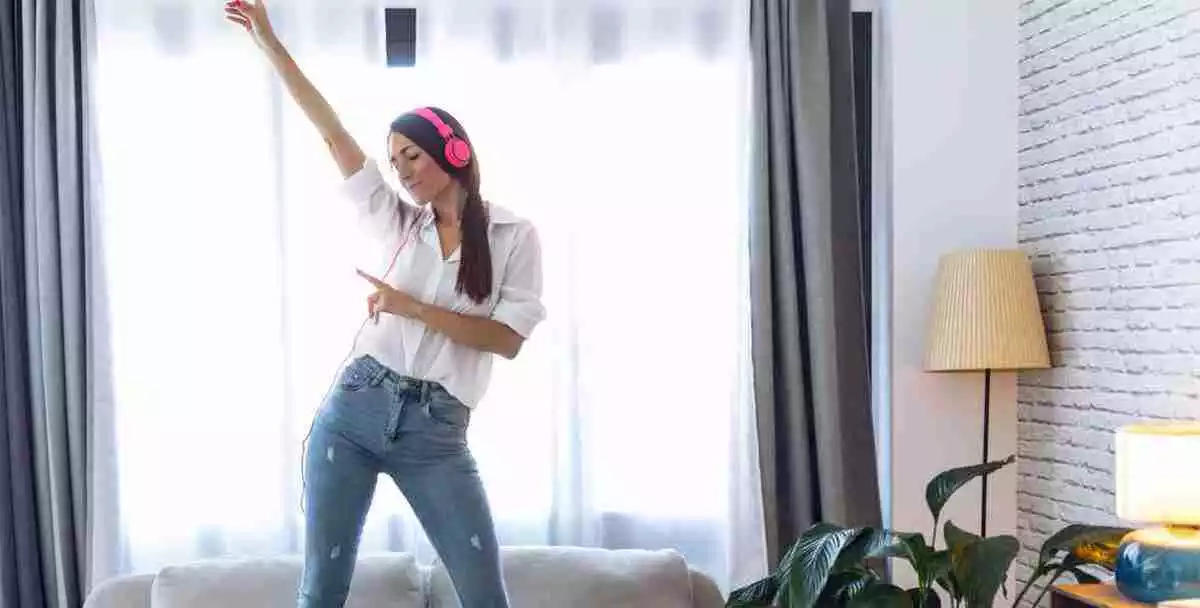 A woman with headphones dancing on the sofa