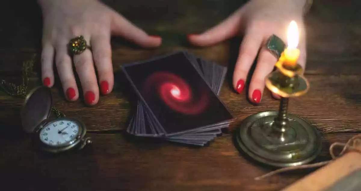 A tarot card deck woth a candle, a watch and two woman's hands