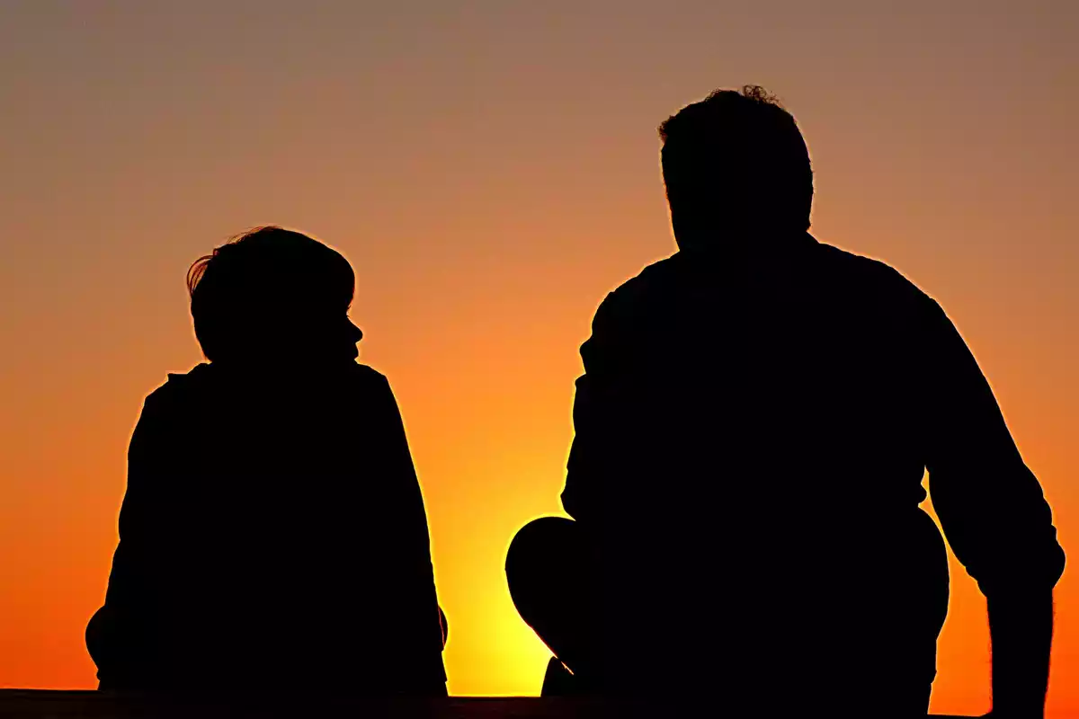 Father and son sitting against the light watching the sunset