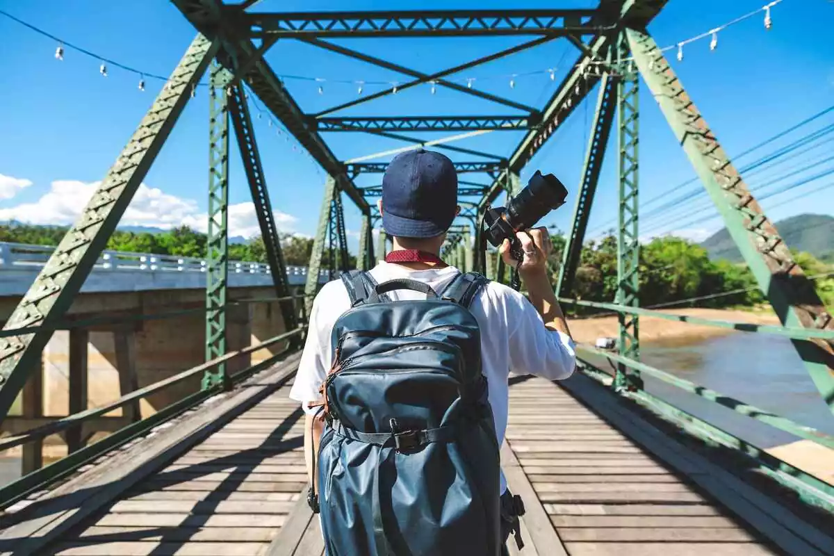 Man holding a camera while crossing a bridge