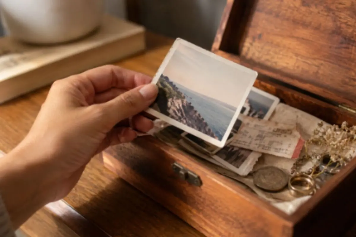Hand holding an old photograph over a wooden box filled with memories and personal belongings. Hand holding an old photograph over a wooden box filled with memories and personal belongings.