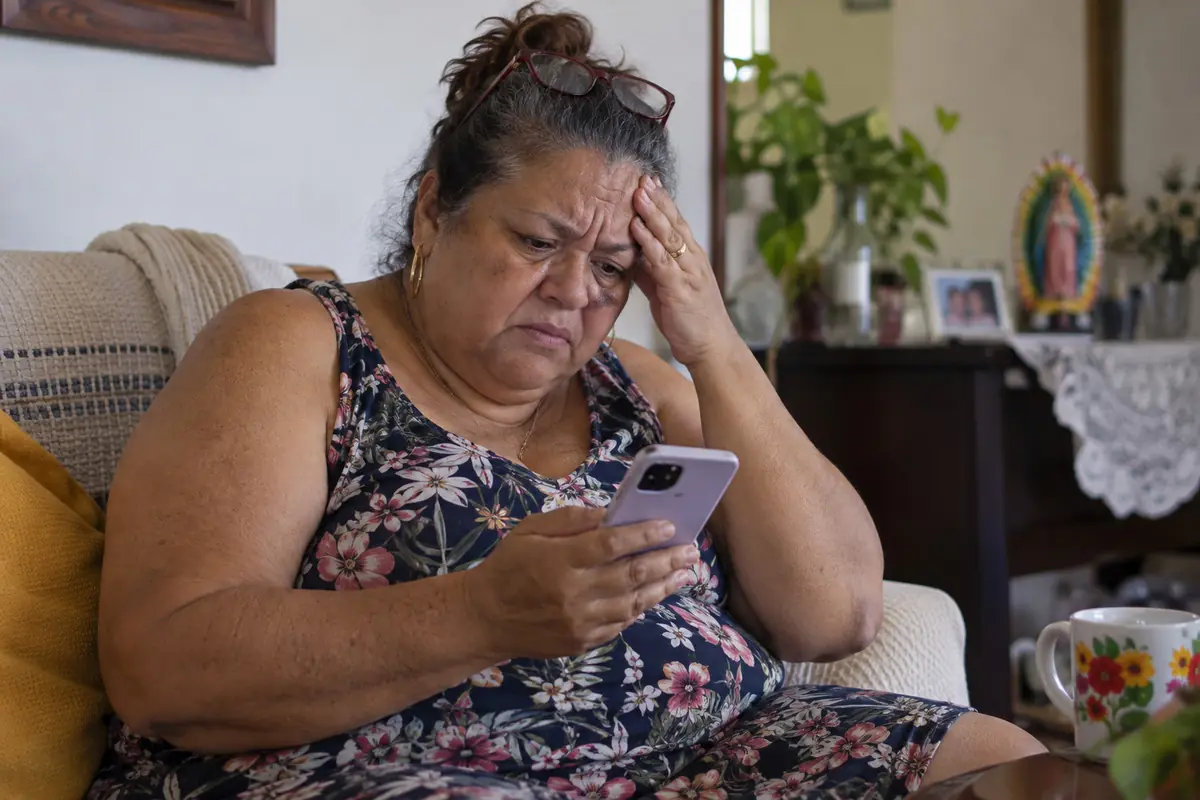 Older woman with a worried expression sitting in an armchair while looking at her mobile phone screen in a living room. Older woman with a worried expression sitting in an armchair while looking at her mobile phone screen in a living room.