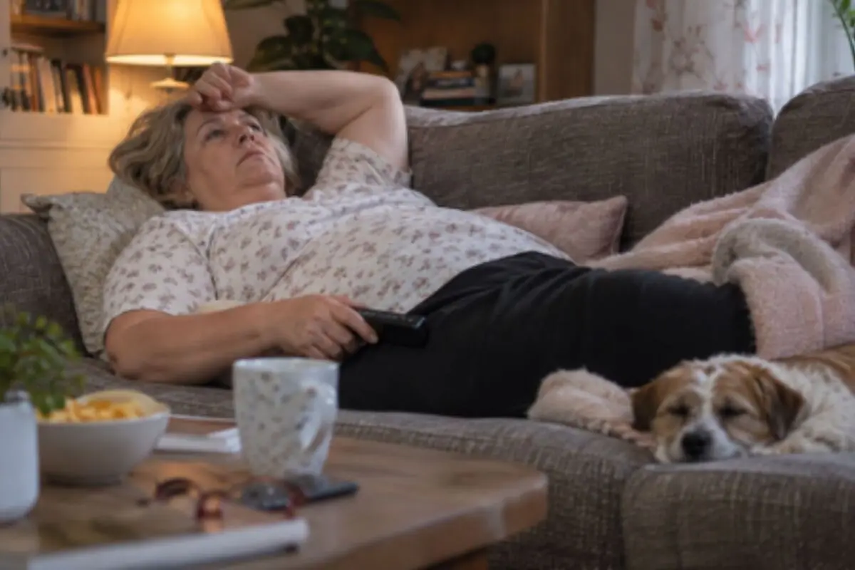 Older woman lying on a sofa with a remote control in her hand next to a sleeping dog in a cozy living room. Older woman lying on a sofa with a remote control in her hand next to a sleeping dog in a cozy living room.