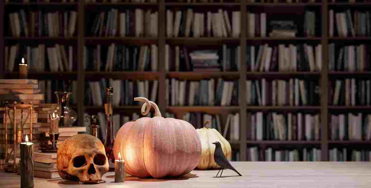 A table with candles, pumpkins and a skull and a library behind it