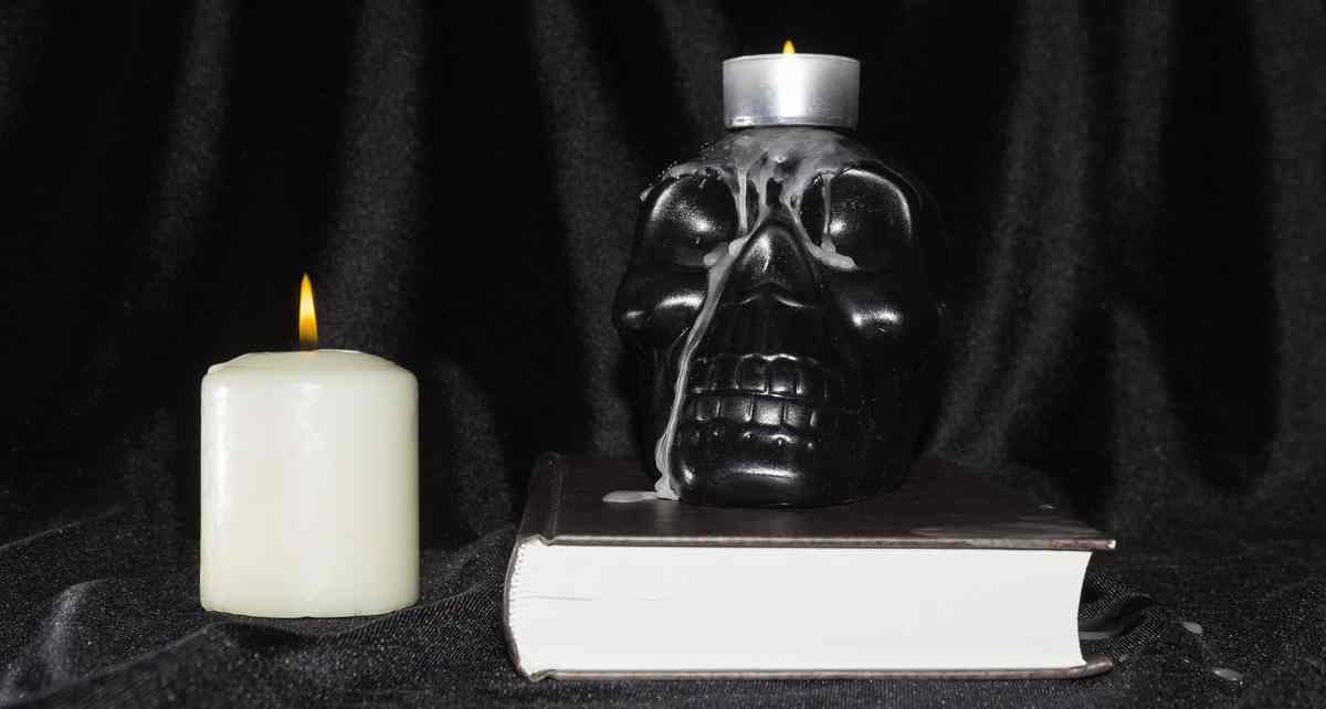 A black skull on a book and with a candle on top of it and next to it